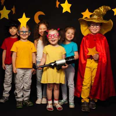 Group of six boys and girls in stargazers costumes watching handmade stars and moon against black background